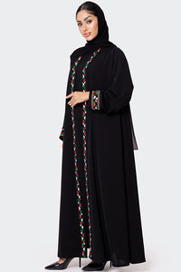 Woman wearing a black abaya with colorful embroidery on a white background