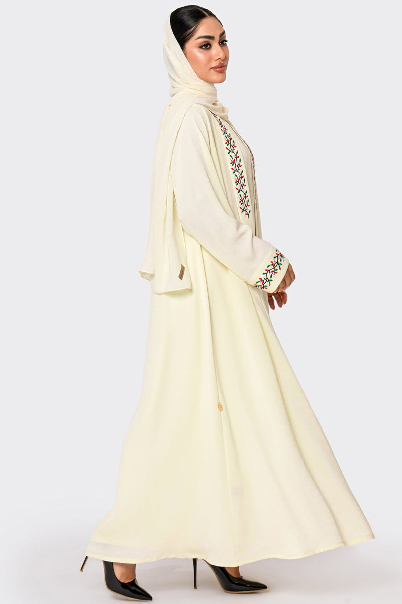 Woman wearing a cream-colored abaya with intricate embroidery on a white background