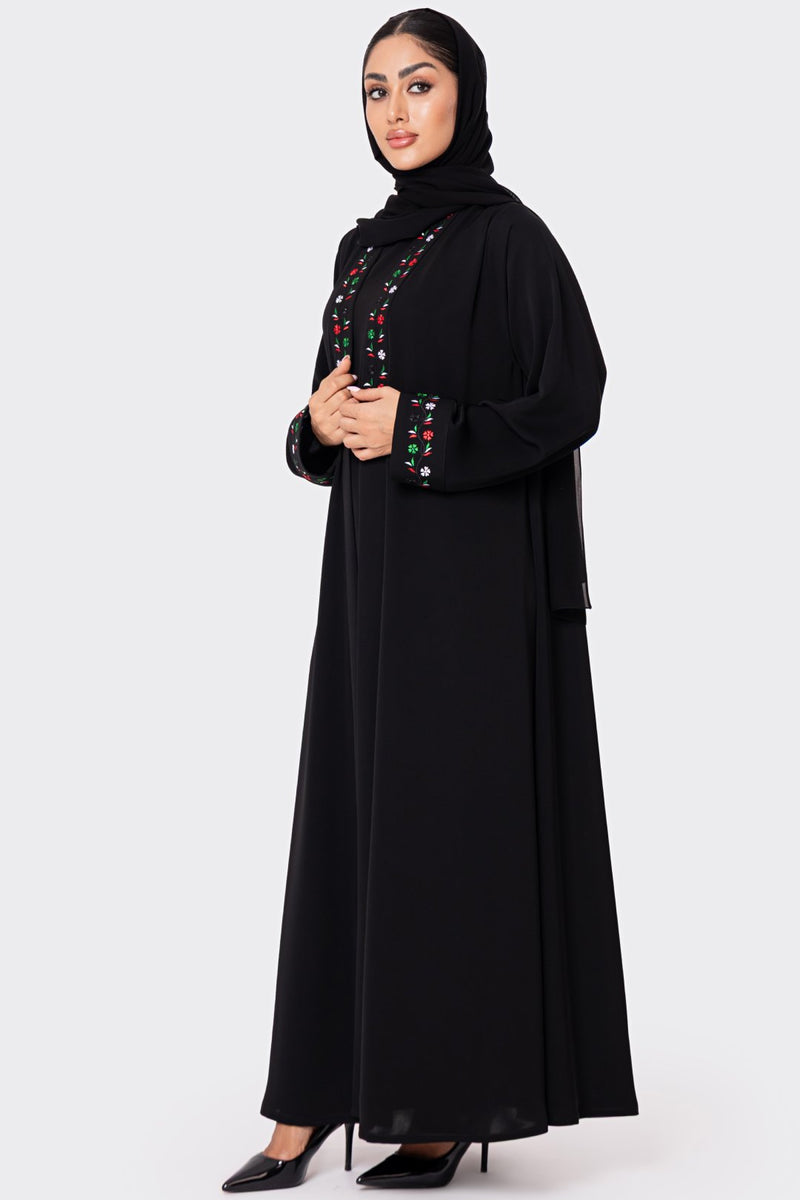 Woman wearing a black abaya with colorful embroidery on a white background