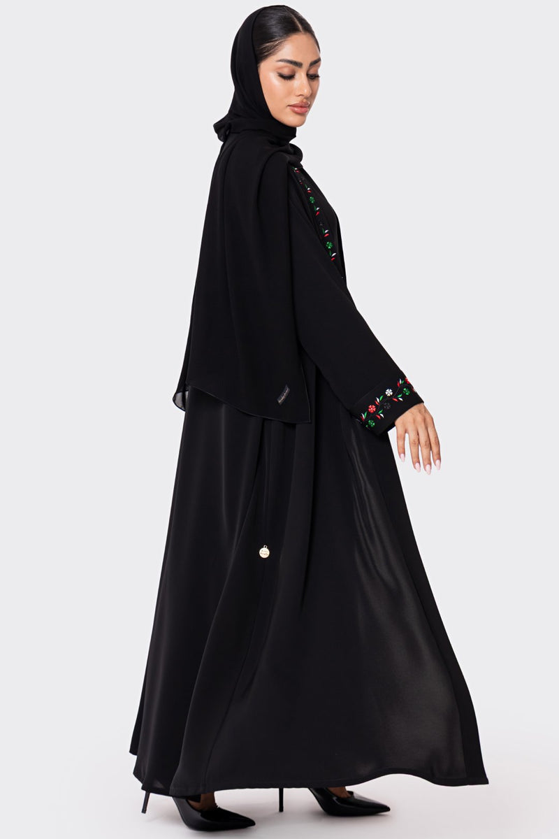 Woman wearing a black abaya with colorful embroidery on a white background