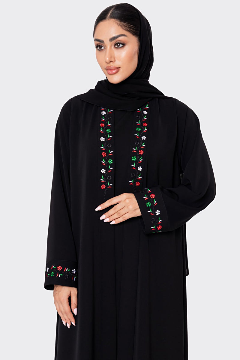 Woman wearing a black abaya with colorful embroidery on a white background