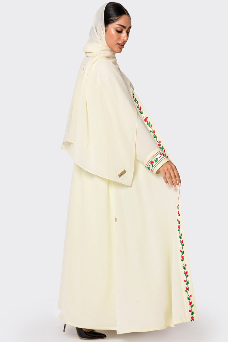 Woman wearing a cream-colored abaya with floral embroidery on a white background