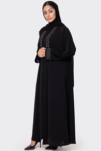 Woman wearing a black abaya with colorful embroidery on a white background