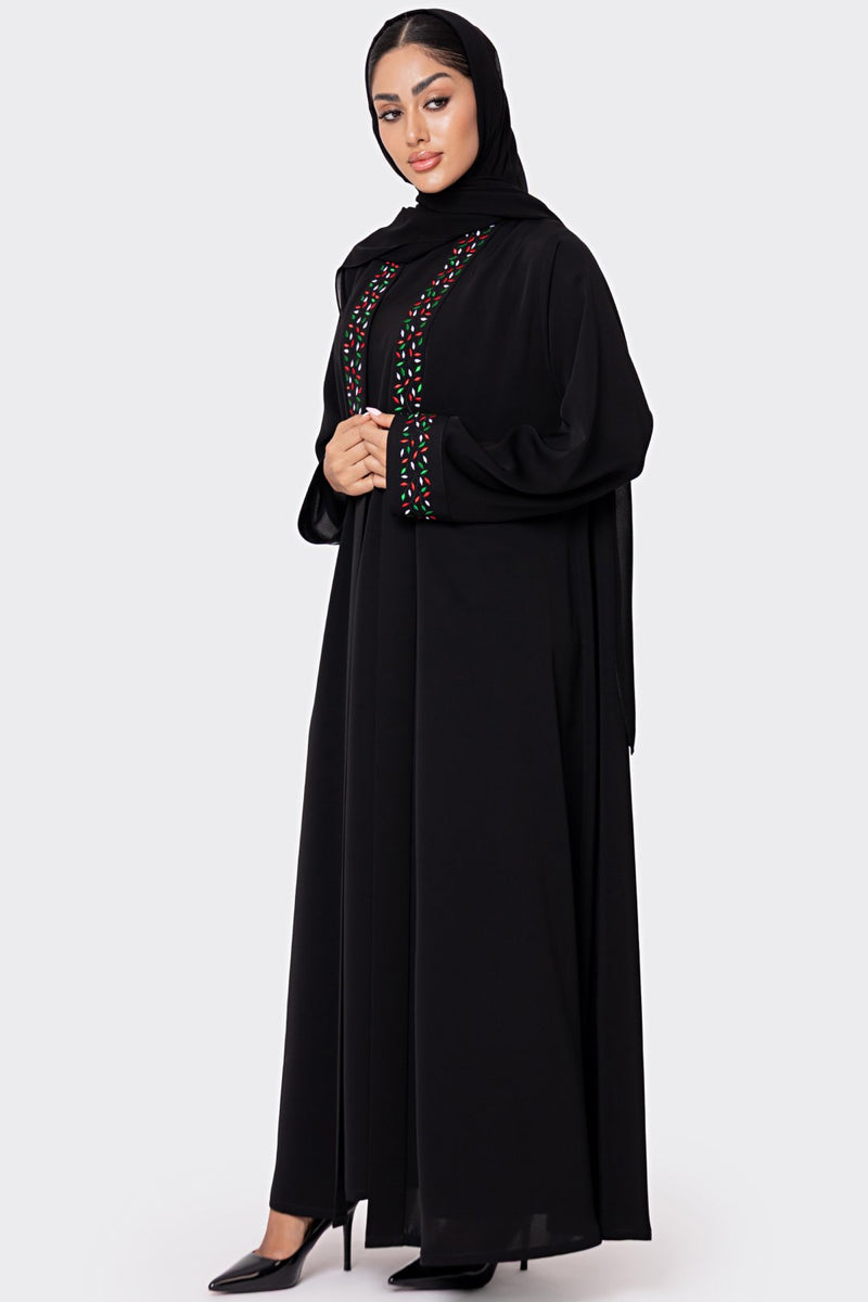Woman wearing a black abaya with colorful embroidery on a white background