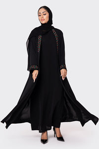 Woman wearing a black abaya with embroidered details on a white background