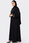 Woman wearing a black abaya with floral embroidery on a white background