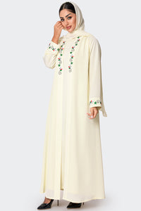 Woman wearing a cream-colored abaya with floral embroidery on a white background