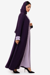 Woman wearing embroidered light and dark purple Fouz Abaya, standing right side elegant pose