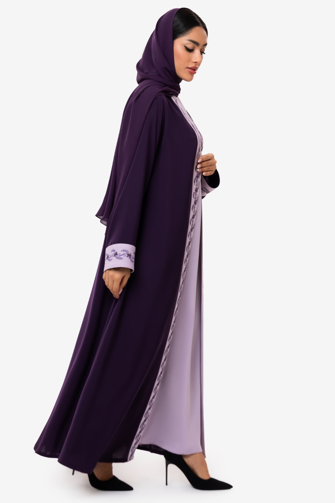 Woman wearing embroidered light and dark purple Fouz Abaya, standing right side elegant pose