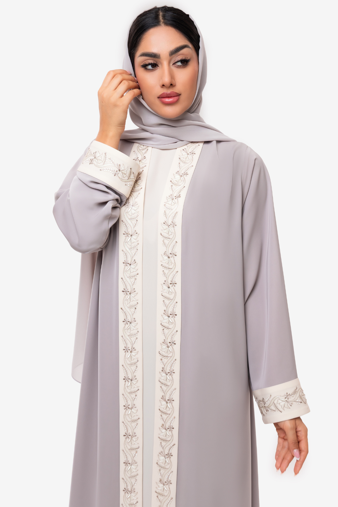 Woman wearing embroidered light beige and off white Nivana Abaya, standing straight