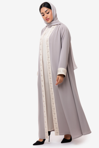 Woman wearing embroidered light beige and off white Nivana Abaya, standing left side elegant pose