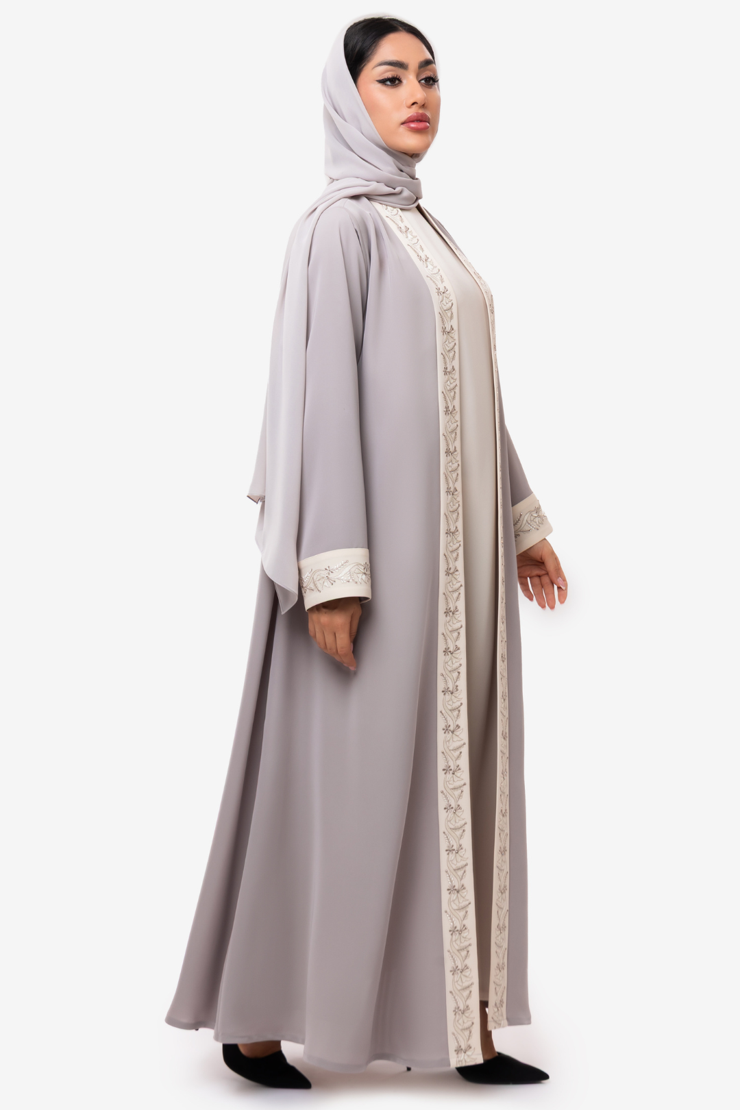 Woman wearing embroidered light beige and off white Nivana Abaya, standing right side elegant pose with straight face