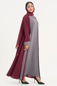 Woman in Noor Abaya, burgundy and grey two-tone abaya, standing right showing side profile and flowy design.